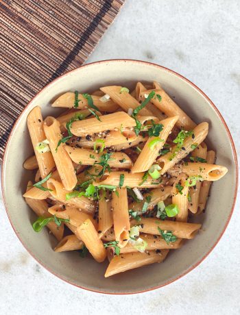 Bowl of penne noodles coated with a rich tahini sesame sauce and garnished with fresh cilantro and green onions.
