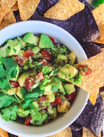 Corn tortilla chips dipped into a bowl of fresh, chunky guacamole made with avocados.