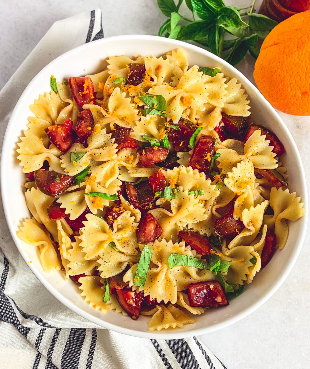 A large bowl of bowtie pasta mixed with fresh heirloom tomatoes, fresh basil, and orange zest.