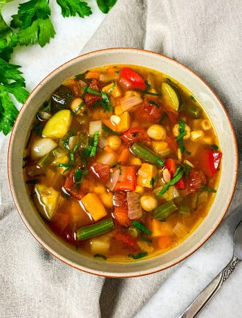 Bowl of vegan vegetable soup packed with green beans, squash, carrots, corn, and tomatoes.
