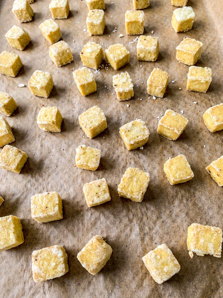 Close up shot of baked tofu cubes on parchment-lined baking sheet.