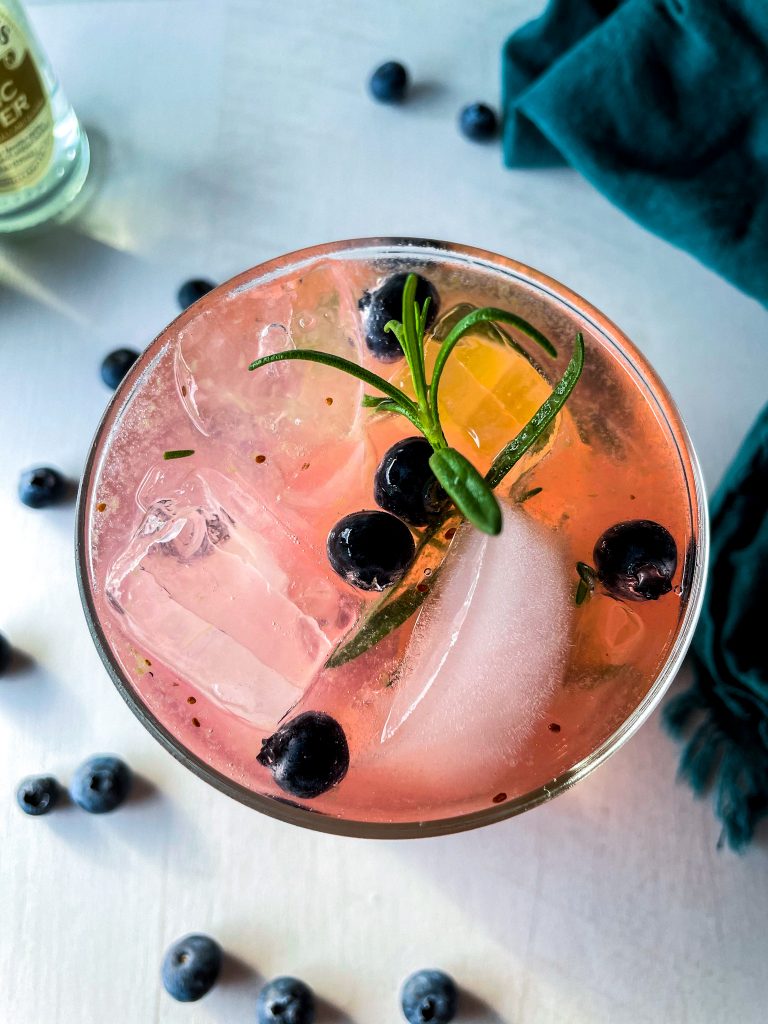 An overhead shot of a blueberry rosemary gin and tonic, garnished with lime.