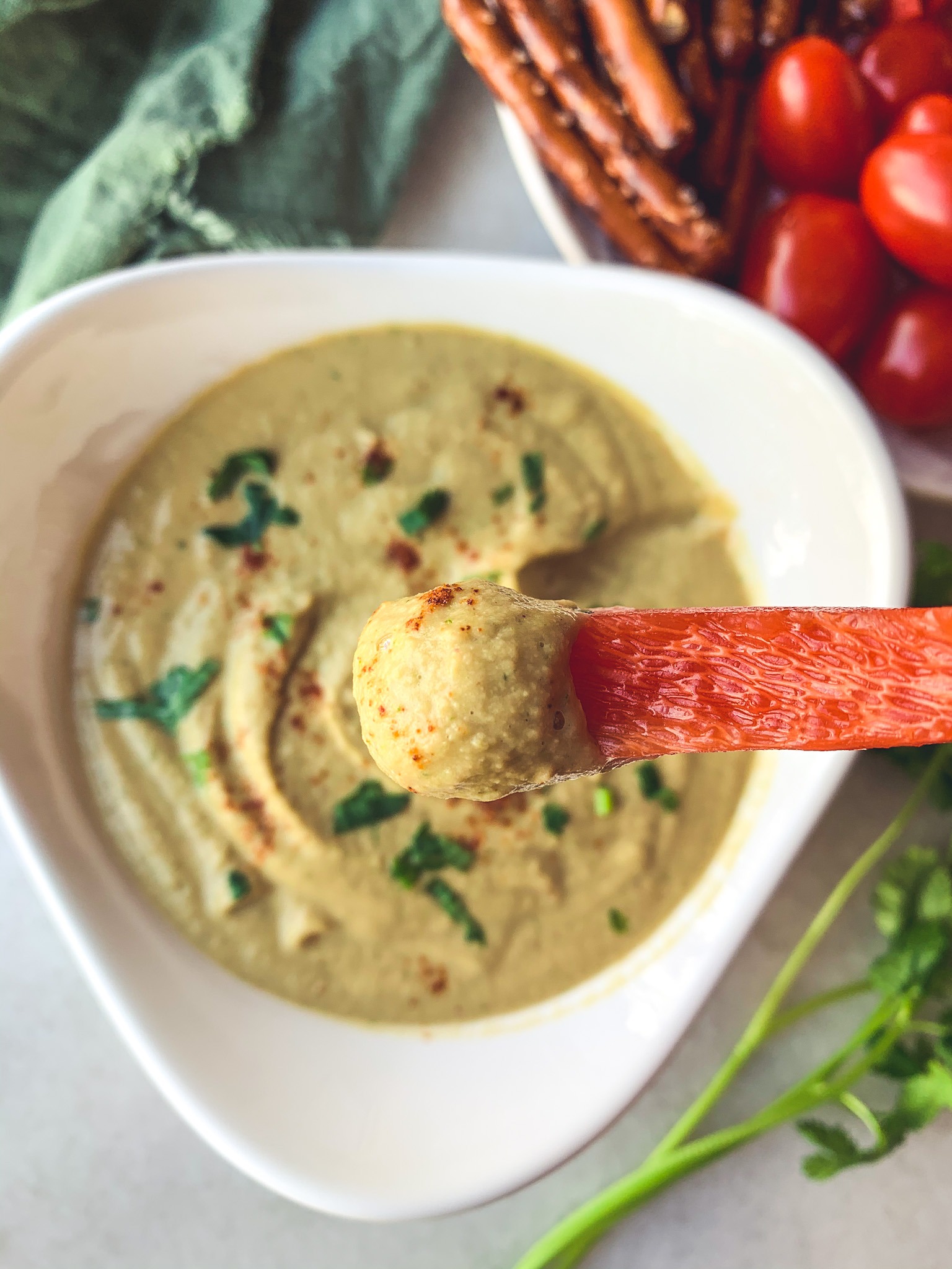 Close-up shot of a red pepper dipped into creamy peanut cilantro hummus with a cayenne garnish.