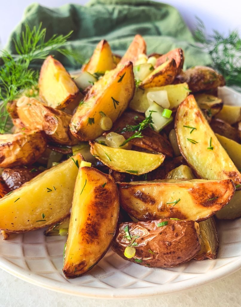 A close up look at a vegan potato salad filled with green onions, fresh dill, and chopped pickles.