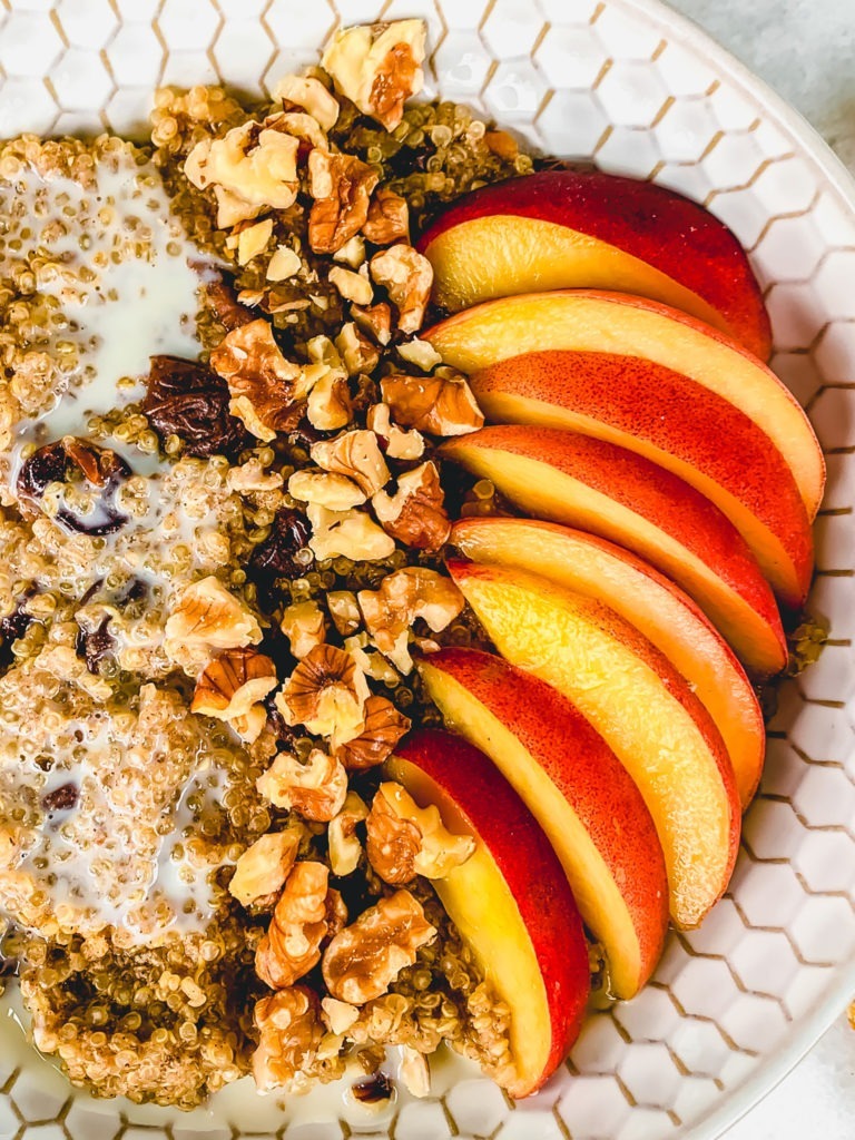 A close up shot of fresh peaches, and toasted walnuts in a hot breakfast quinoa bowl.
