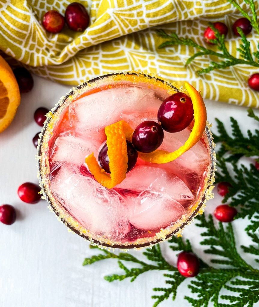 Overhead view of a holiday beverage with fresh cranberries, ginger beer, and an orange sugar rim.