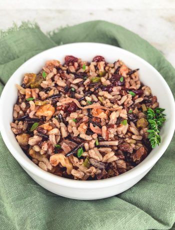 A bowl of vegan wild rice pilaf featuring shallots, toasted walnuts, and cranberries.
